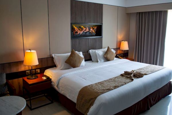 A cozy hotel room with a double bed, two bedside lamps, decorative pillows, and a wall-mounted decor piece above the bed.