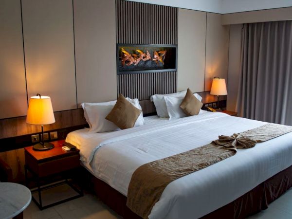A cozy hotel room with a double bed, two bedside lamps, decorative pillows, and a wall-mounted decor piece above the bed.