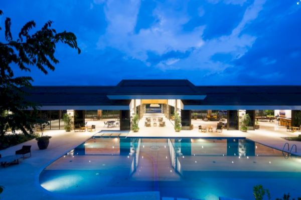 A beautiful building with large glass windows and a swimming pool is illuminated under a twilight sky.