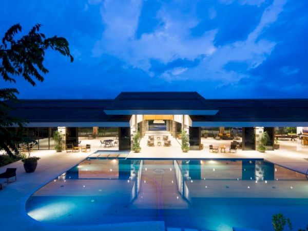 A beautiful building with large glass windows and a swimming pool is illuminated under a twilight sky.