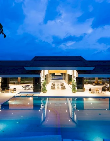 A luxurious, illuminated building with a large pool in front, set against a twilight sky, creating a serene and inviting atmosphere.