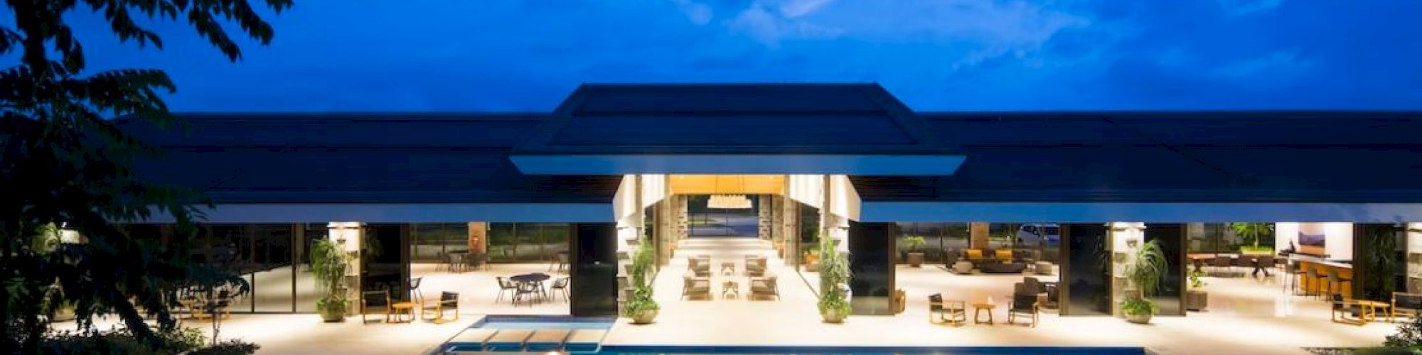 A luxurious pool area in front of a modern building, illuminated at dusk with a clear sky backdrop, creating a serene and inviting atmosphere.