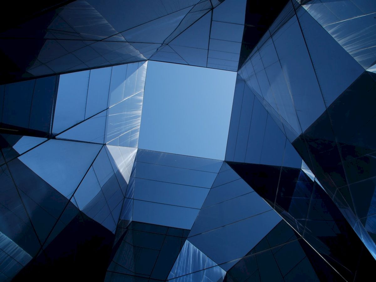Architectural view upward through reflective glass buildings forming a geometric pattern with blue sky visible in the center.