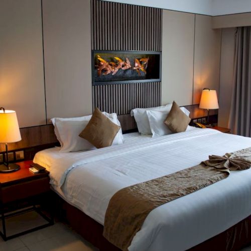 A cozy hotel room with a large bed, warm lighting, and elegant decor, featuring side tables and a modern art piece above the headboard.