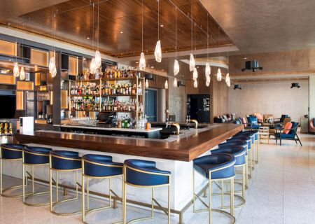 Sophisticated bar with elegant lighting, stocked shelves, blue cushioned stools, and modern decor in a spacious, inviting room.