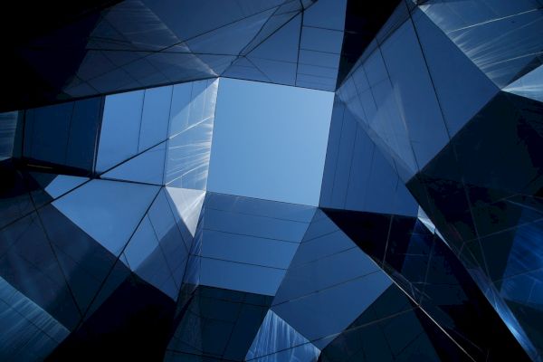 Geometric architecture with reflective glass panels forms a pattern against the sky, creating a visually striking, abstract design.