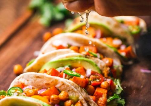 A hand squeezes lime over tacos filled with chickpeas, avocado, and vegetables, garnished with cilantro on a wooden board.