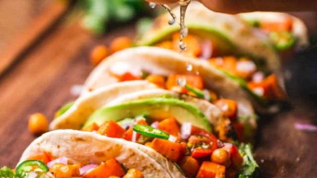 A hand squeezes lime over tacos filled with chickpeas, avocado, and vegetables, garnished with cilantro on a wooden board.