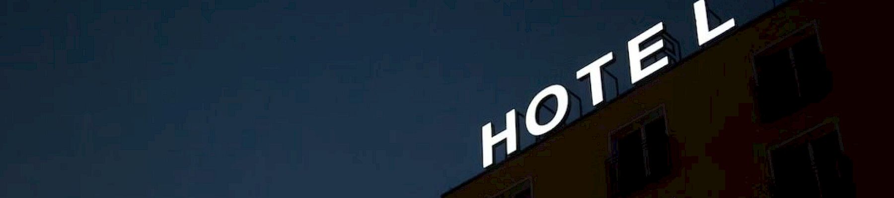 A building at night with a sign reading "HOTEL" is depicted, missing a single letter "E" on its rooftop.