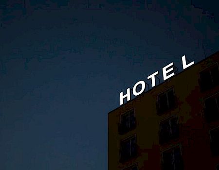 A building at night with a sign reading "HOTEL" is depicted, missing a single letter "E" on its rooftop.