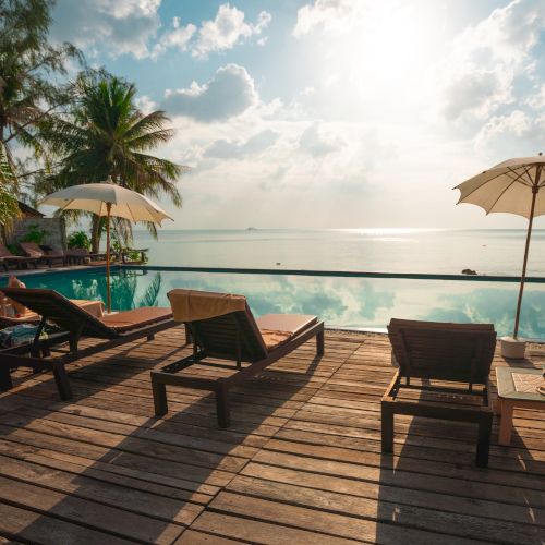 A serene poolside with lounge chairs and umbrellas, overlooking a calm sea under a bright sky with scattered clouds.