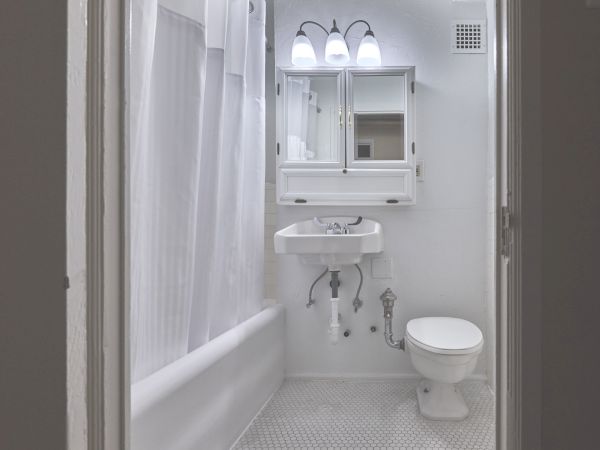 A small, white bathroom with a toilet, sink, mirrored cabinet, and a shower curtain around the bathtub is depicted in the image.