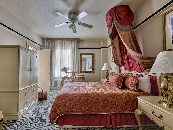 A luxurious bedroom with ornate decor, featuring a draped canopy bed, elegant furniture, and a zebra-patterned rug on the floor.