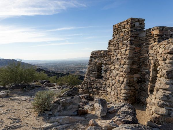 Ancient stone ruins in a desert landscape, with mountains and clear sky visible in the background, creating a serene and timeless scene.