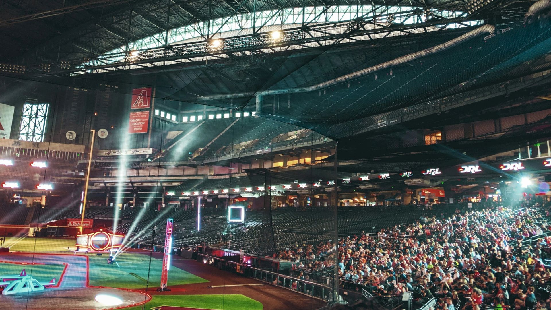 An indoor arena with a large audience, illuminated stage, and colorful lights, possibly hosting a drone racing event.