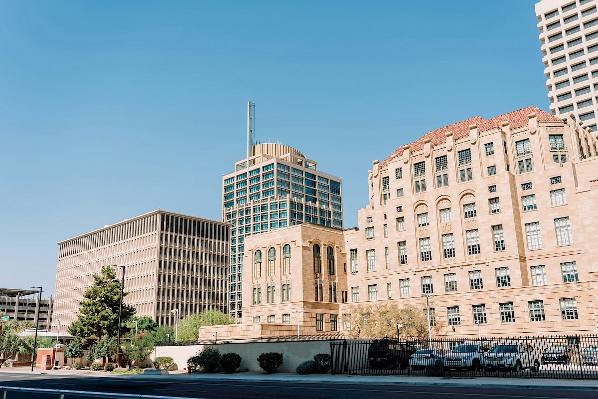 The image shows a cityscape with several tall buildings, clear skies, and a few parked cars along the street.