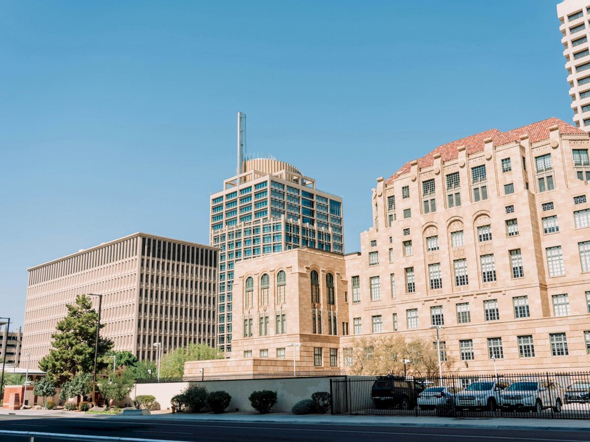 The image shows a cityscape with several tall buildings, clear skies, and a few parked cars along the street.