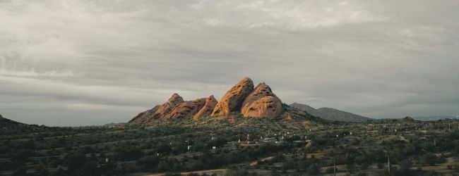 A desert landscape with rock formations and a cloudy sky, surrounded by sparse vegetation.