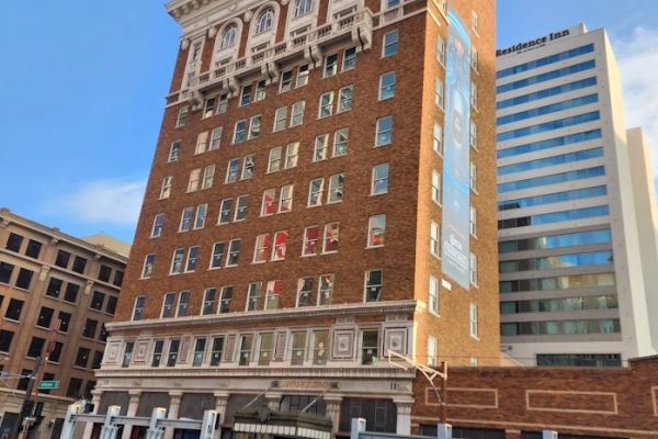 A historic multi-story brick building with decorative elements stands prominently, flanked by modern structures in the city.