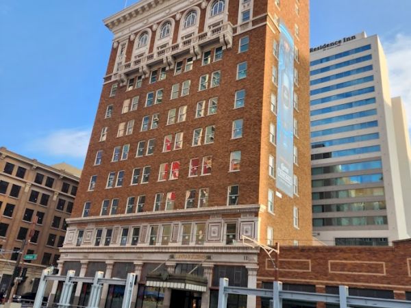 A historic multi-story brick building with decorative elements stands prominently, flanked by modern structures in the city.
