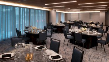 Elegant banquet hall with round tables set for an event; dim lighting, floral centerpieces, and neatly arranged cutlery.