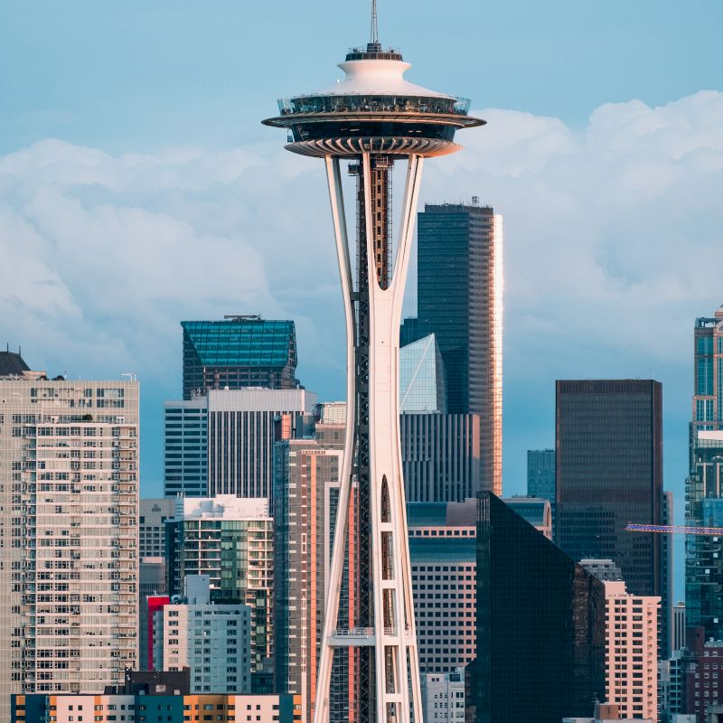 The image shows a city skyline with a tall, iconic tower featuring a disk-shaped structure near the top against a backdrop of skyscrapers.