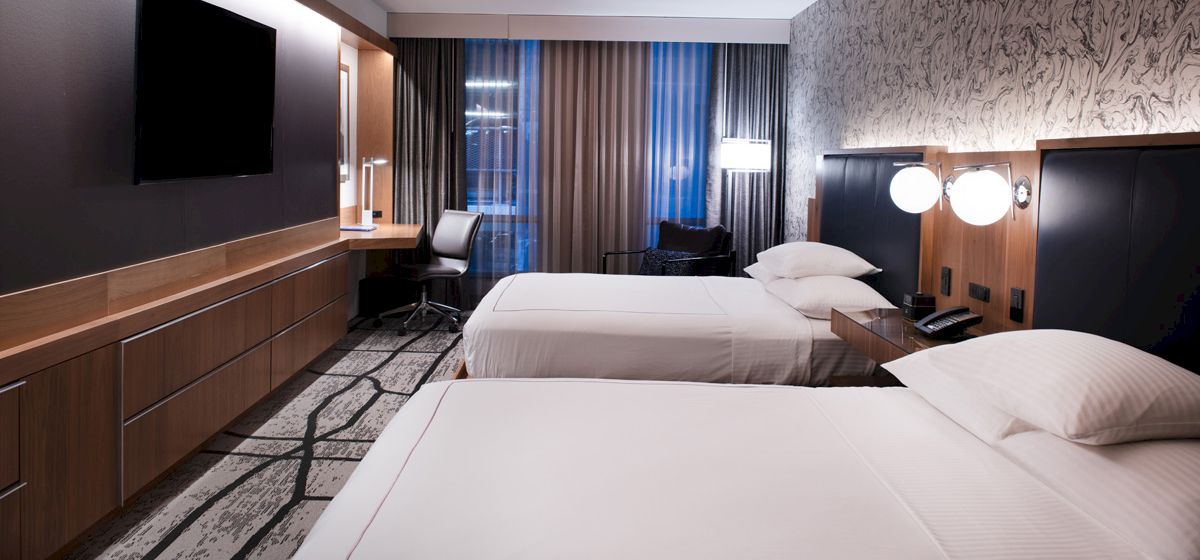 The image shows a hotel room with two double beds, modern decor, a desk, chair, wall-mounted TV, and patterned carpet ending the sentence.