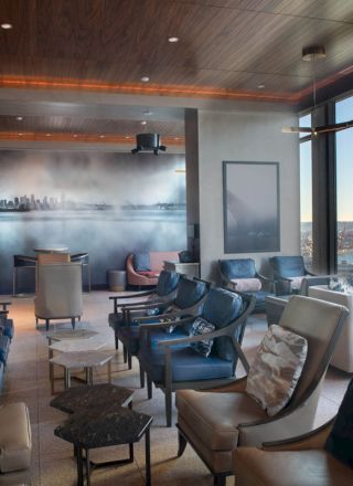 A modern lounge with comfortable seating, large windows revealing a waterfront view, and a city skyline mural on one wall.