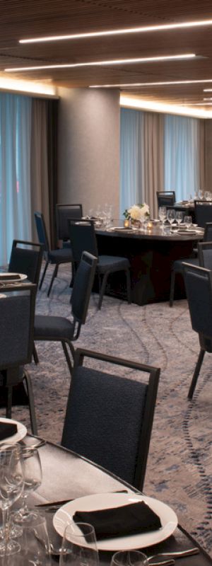 The image shows an elegant dining room with round tables set for an event, featuring blue chairs and ambient lighting.