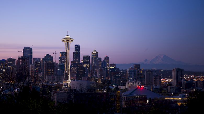 Seattle skyline at dusk showing the Space Needle, city buildings, and Mount Rainier in the background against a clear sky.