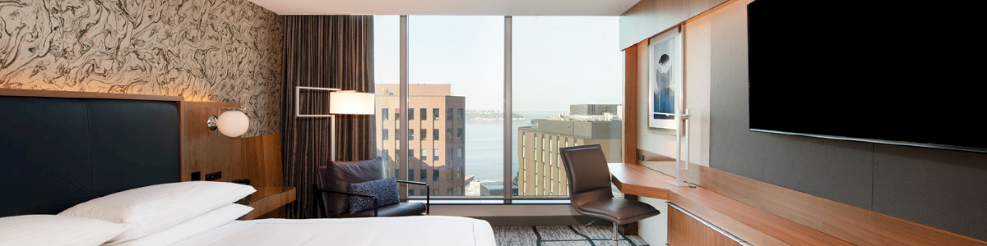 A modern hotel room featuring a large bed, flat-screen TV, desk with chair, stylish decor, and a window with a cityscape view ends the sentence.
